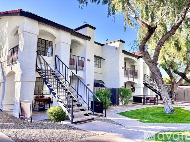 A white building with a red roof and a tree in front.