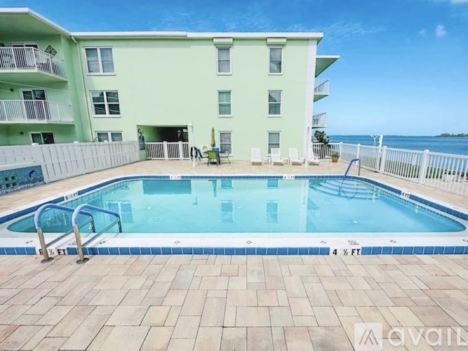 A pool in front of a light green building with a white fence around it.