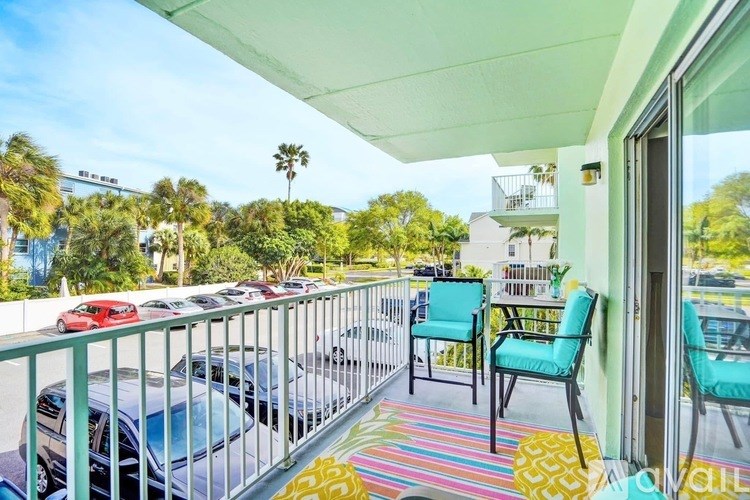 A balcony with a striped rug and two chairs overlooks a parking lot.