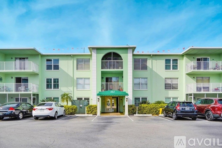 A row of green apartment buildings with cars parked in front.