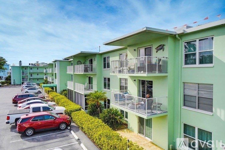 A row of green apartment buildings with cars parked in front.