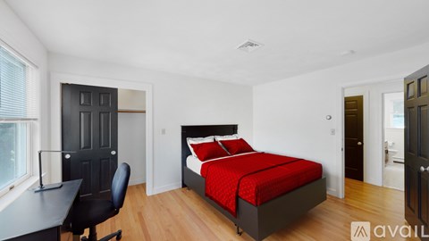 A bedroom with a red bed and a black desk.