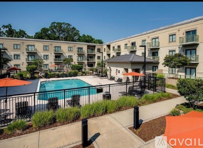 A swimming pool surrounded by a black fence and orange umbrellas in front of a building.