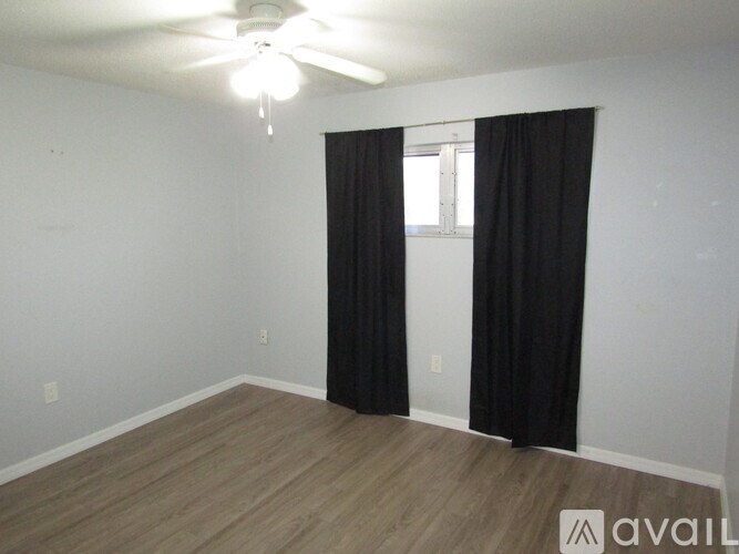 A room with a ceiling fan and a window with black curtains.