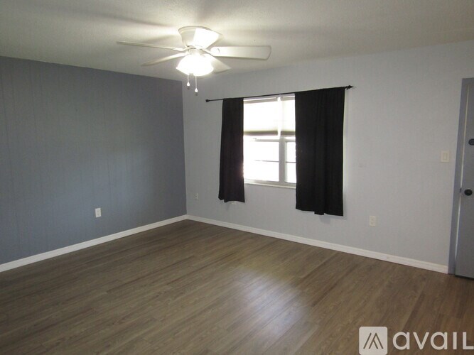 A room with a ceiling fan and a window with black curtains.