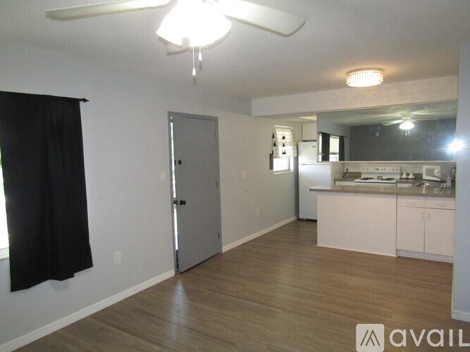 A room with a ceiling fan and a kitchen area in the background.