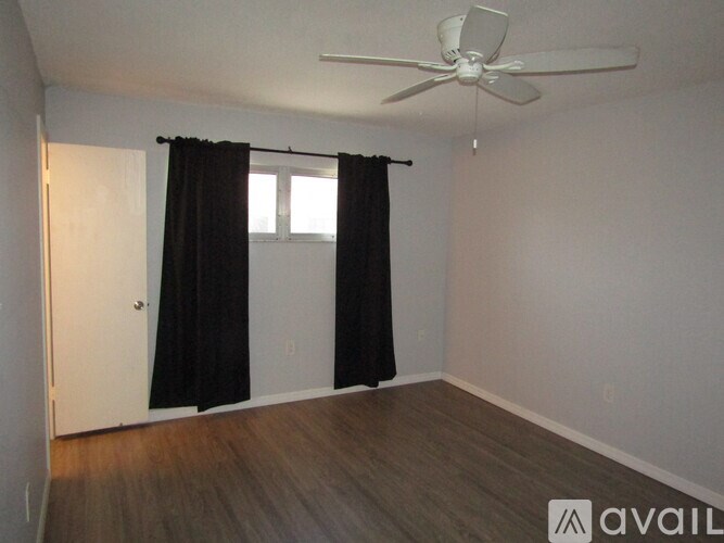 A room with a ceiling fan and a window with black curtains.