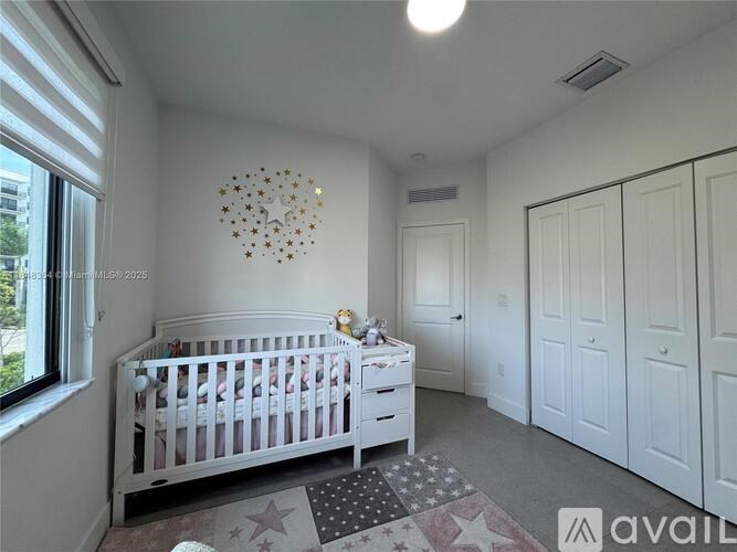A white crib with a star-shaped decoration on the wall and a window with blinds on the left side.