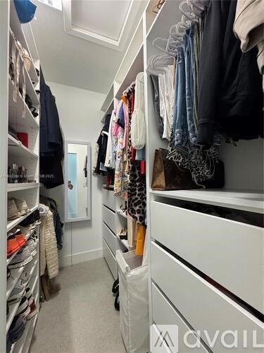 A walk in closet with clothes hanging on shelves and drawers.
