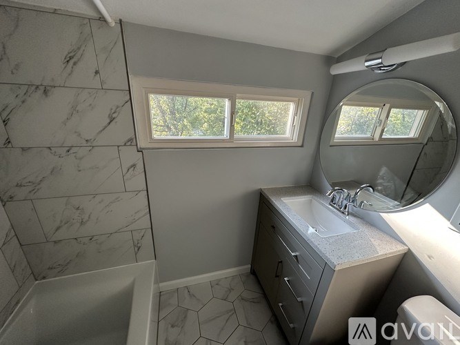 A bathroom with a marble tiled shower and a vanity with a round mirror.
