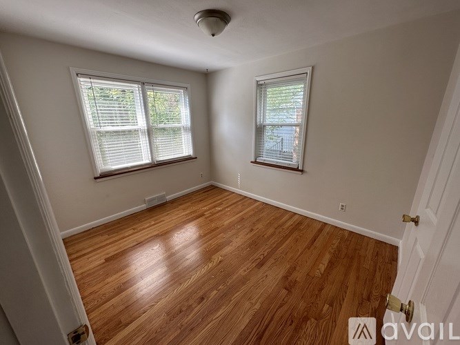 A room with wooden flooring and two windows.