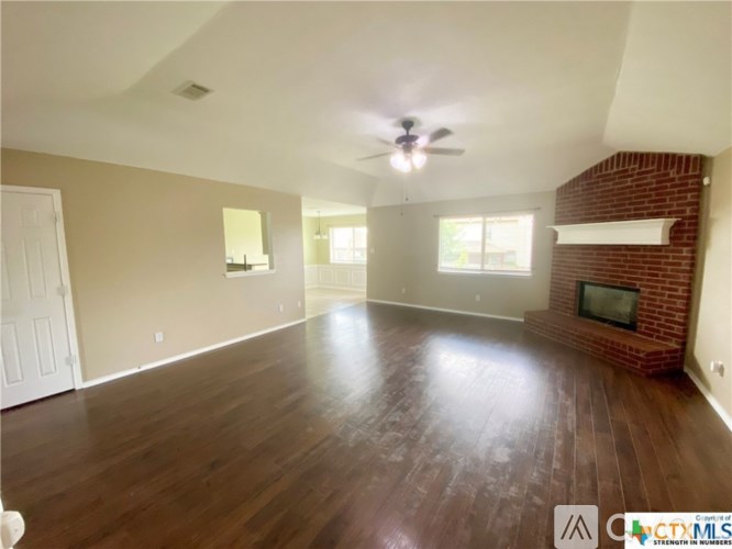 A spacious living room with a brick fireplace and hardwood floors.