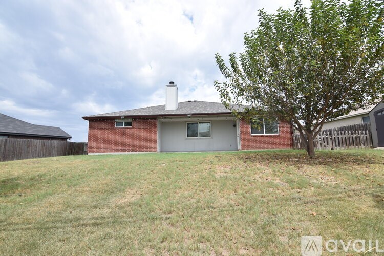 A house with a red brick exterior and a grey roof is surrounded by a grassy area and a tree.