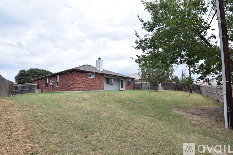 A house with a brown roof and a grey garage door is surrounded by a fence and a grassy yard.