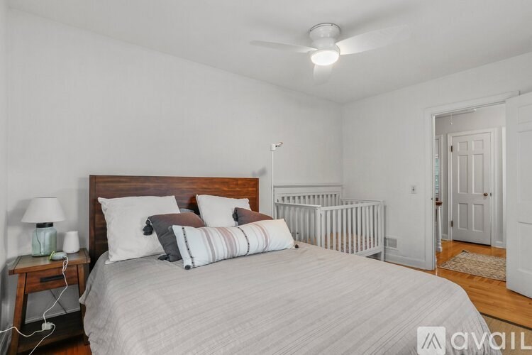 A bedroom with a bed, a nightstand with a lamp, and a baby crib.