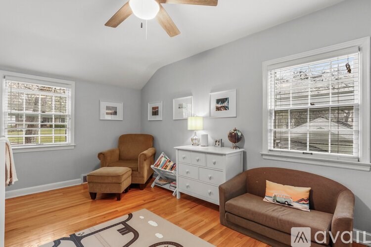A living room with a brown couch, a chair, a dresser, and a ceiling fan.