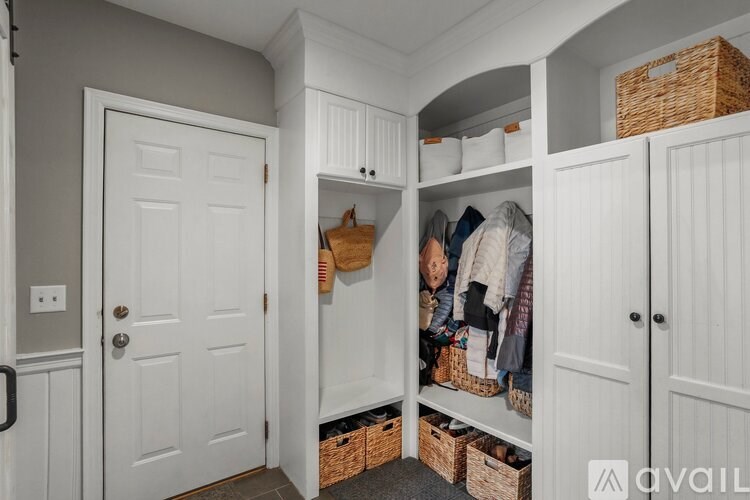 A hallway with a white door and a white cabinet with clothes and baskets.
