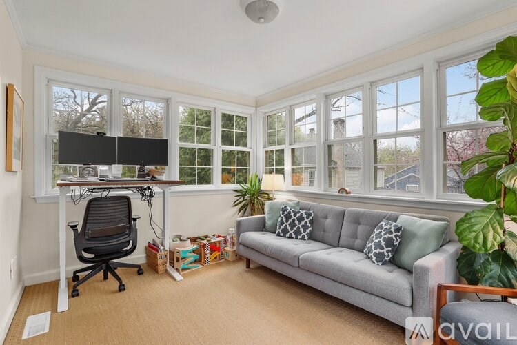 A sunny room with a grey couch, a black chair, and a desk with a computer.