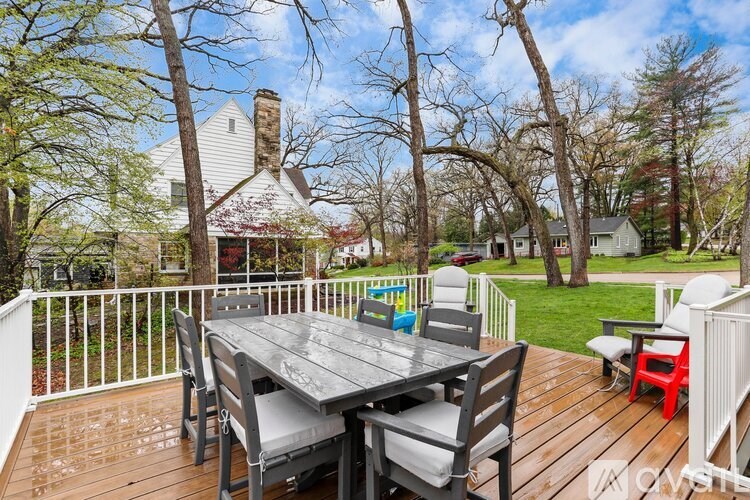 A wooden table with chairs is on a deck with a white railing.