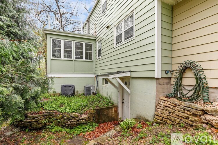 A green shed sits next to a house with a hose hanging on the wall.