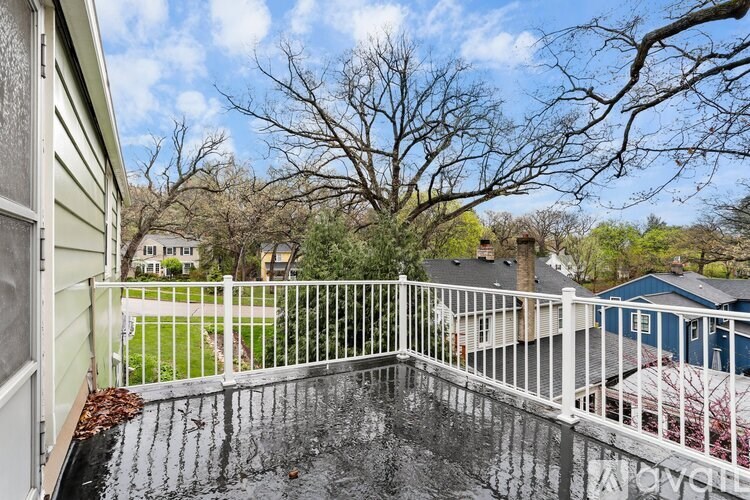 A wet balcony with a white railing and a tree in the background.