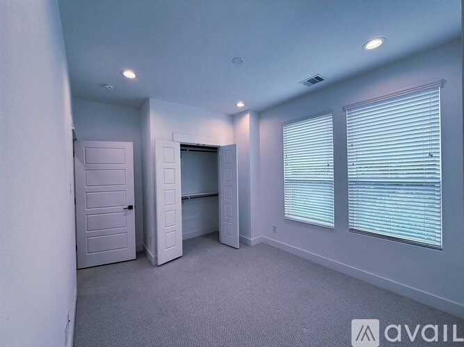 A room with a carpeted floor, a door, and a window with blinds.