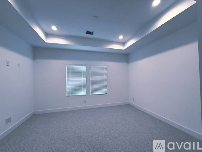 A room with a carpeted floor, a window with blinds, and a ceiling with recessed lighting.