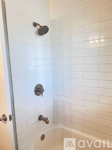 A white tiled shower with a glass door and a shower head and faucet.