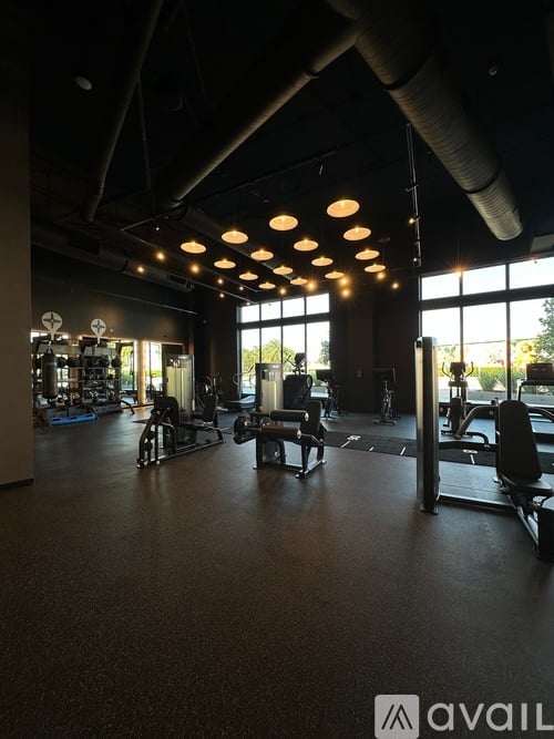 A gym with various exercise equipment and a large window letting in natural light.