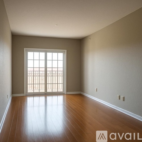 A room with wooden floors and a large window with a view of a balcony.