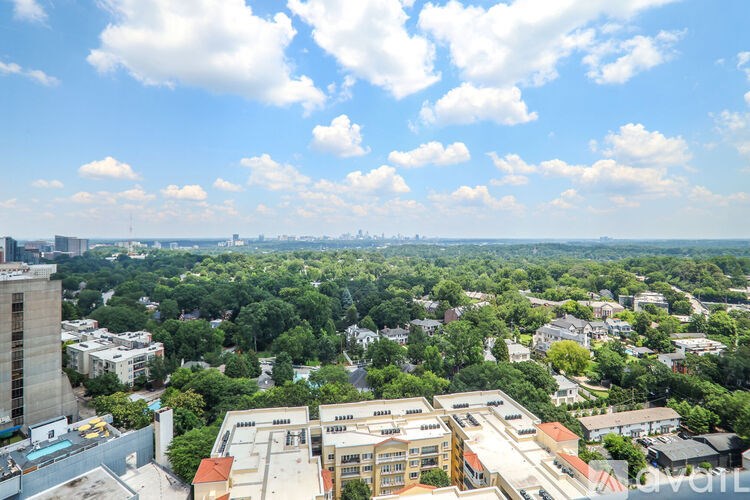 A cityscape with buildings and trees under a blue sky with clouds.