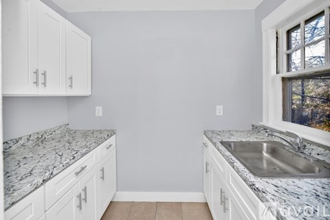 A kitchen with white cabinets and marble countertops.
