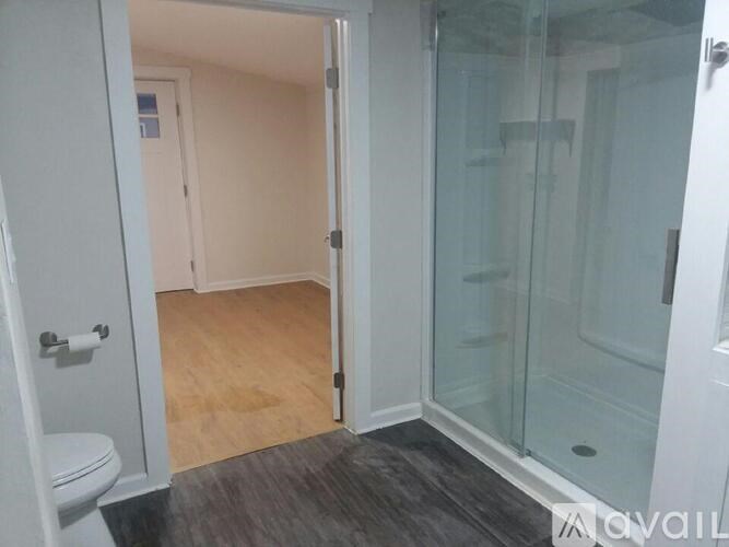 A bathroom with a toilet, a glass shower door, and a wooden floor.