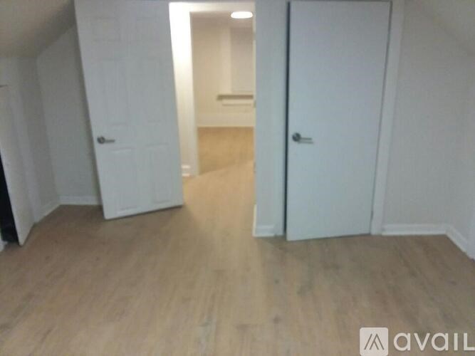 A room with wooden floors and white walls, with two doors visible.