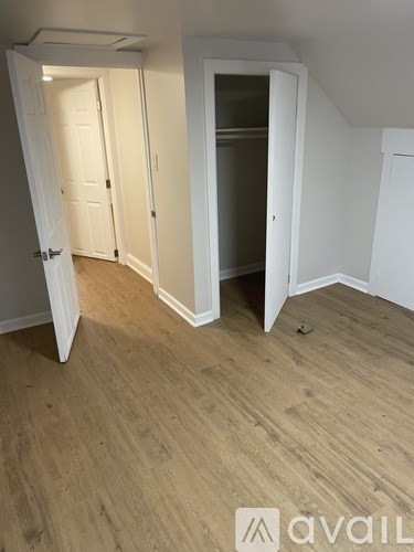 A room with a wooden floor and white walls, with a door open to another room.