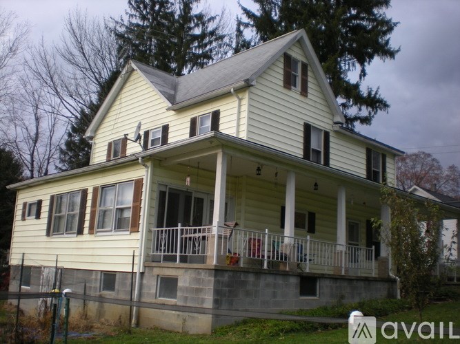 A yellow house with a porch and a fence in front.