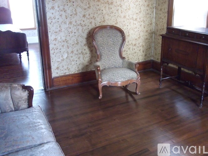 A chair with a floral patterned cushion sits in a room with wooden floors and furniture.