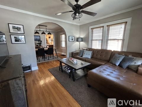 A living room with a brown leather couch and a ceiling fan.