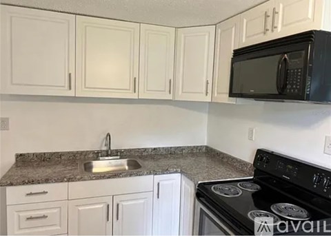 A kitchen with white cabinets and a black microwave above the stove.