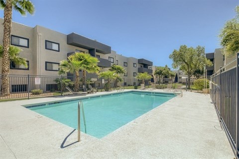 A swimming pool in front of a building surrounded by palm trees.