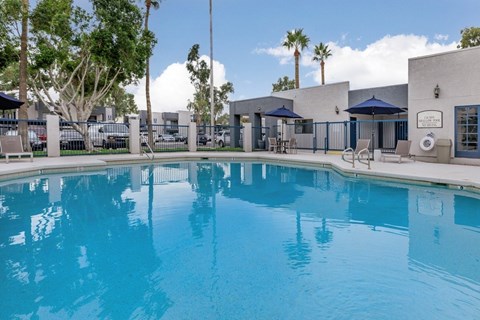 A large swimming pool in front of a building with a blue sky and palm trees in the background.
