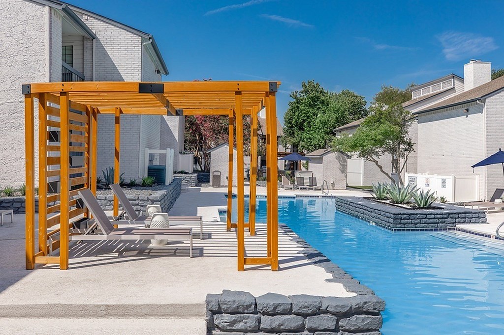 A pool with a wooden pergola and a stone wall.