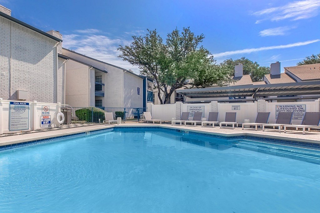 A swimming pool in front of a building with a tree in the background.