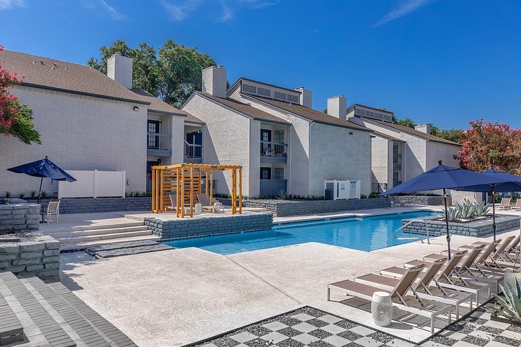 A pool area with sun loungers and a building in the background.