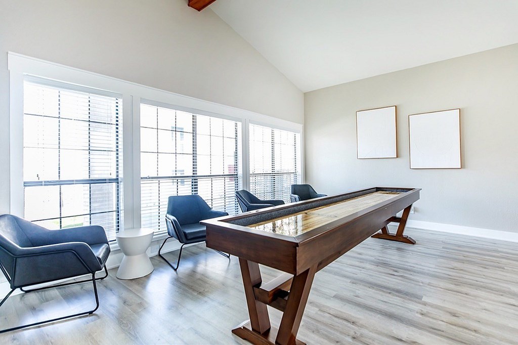 A pool table is in the middle of a room with two chairs and two picture frames on the wall.