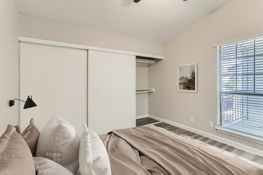 A bedroom with a bed, pillows, and a window with blinds.