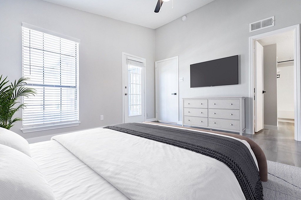 A bedroom with a large bed and a flat screen TV mounted above a cabinet.