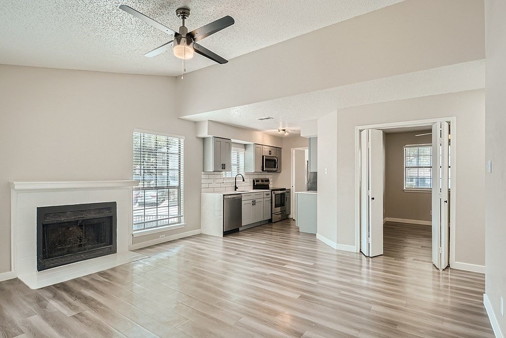 A living room with a fireplace and a kitchen in the background.