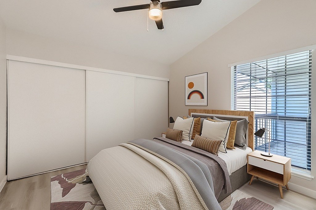 A bedroom with a bed, a ceiling fan, and a window with blinds.