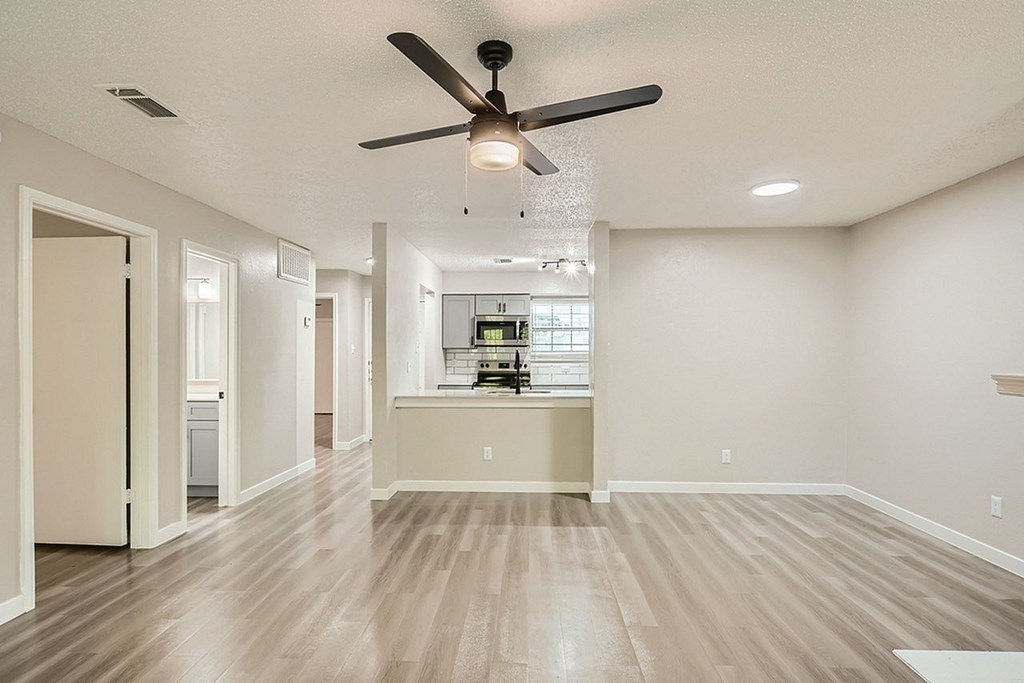 A spacious room with a ceiling fan and a kitchen area in the background.